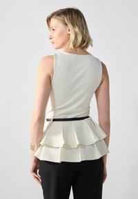 Kremasti peplum top u figurnom kroju, s višeletnim volanima na rubu i crnim remenom. Glatka tkanina i bez rukava.