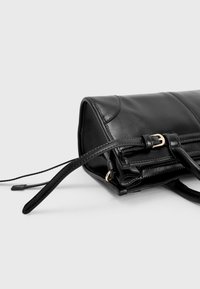 Zwarte leren handtas met een gestructureerd ontwerp, voorzien van gouden metalen accenten, een gladde textuur en verstelbare riemen.