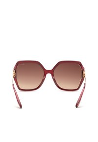 Lunettes de soleil hexagonales surdimensionnées avec montures rouges translucides et verres dégradés marron, avec charnières décoratives ton or.