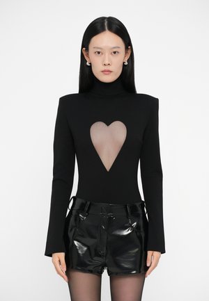 Zwart fitted bodysuit met lange mouwen, voorzien van een hartvormige doorzichtige uitsnede op de borst, gecombineerd met glanzende zwarte shorts.