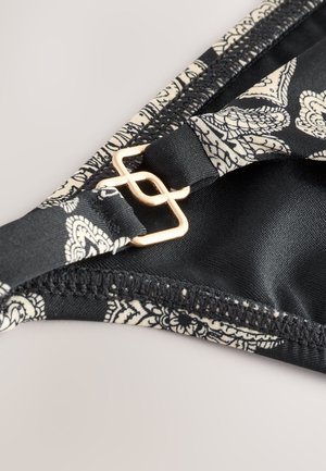 Černý horní díl bikin s květinovým vzorem v krémové barvě, vybavený zlatou sponou a hladkou texturou látky podél okrajů.