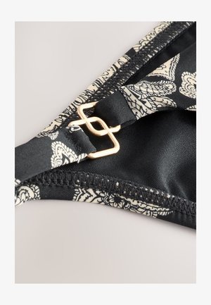 Melns bikini tops ar ziedu rakstu krēmkrāsā, tam ir zelta apdare ar aizdari un gluda auduma tekstūra malas daļās.