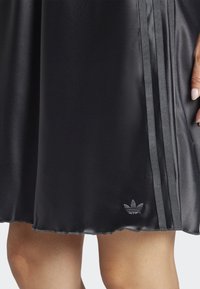 Black athletic dress featuring satin-like material, two side stripes in darker black, and a small embossed logo near the hem.