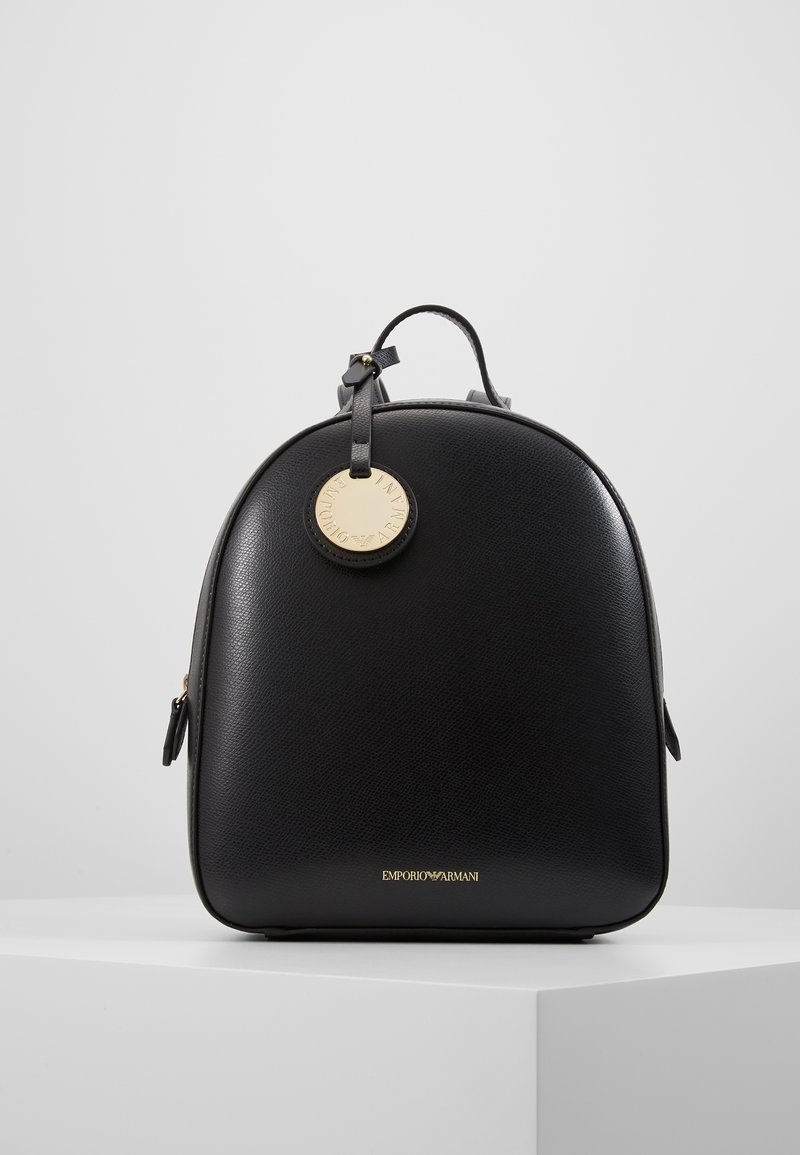 Mochila de cuero negro con forma redondeada, que presenta una etiqueta de logo en dorado, cierres de cremallera y un acabado texturizado. El nombre de la marca está grabado en la parte inferior.