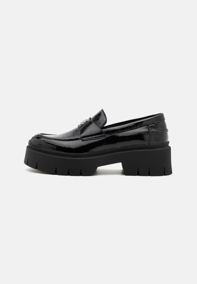 Mocassin en cuir verni noir avec une semelle plateforme épaisse et une bande de roulement crantée, équipé d'un emblème métallique décoratif sur l'empeigne.