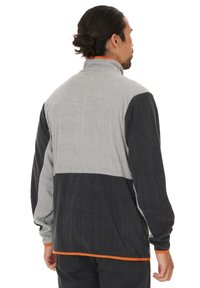 Giacca in fleece grigia e nera con colletto alto, caratterizzata da accenti arancioni lungo il colletto e l'orlo; tessuto testurizzato, design a blocchi di colore.