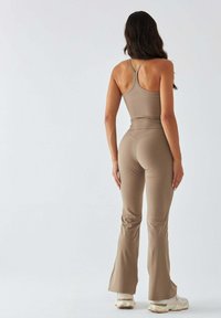 Tan activewear set featuring a fitted tank top with thin straps and flared leggings, all in a smooth, stretchy material.