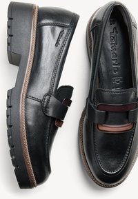 Paire de mocassins en cuir noir avec semelles épaisses et ferrures rectangulaires décoratives à l'avant, taille 37, marque Tamaris.