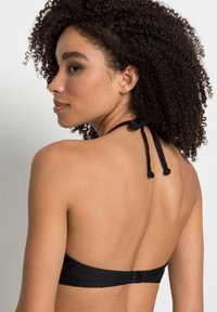Top bikini nera con un motivo testurizzato, con legacci al collo e chiusura sulla schiena. Presenta un design monocromatico uniforme.