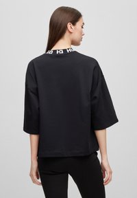 T-shirt nera oversize con maniche a tre quarti, caratterizzata da un dettaglio logo bianco lungo il colletto. Tessuto liscio e vestibilità rilassata.