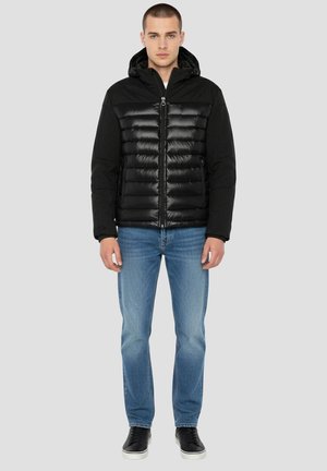 Czarna kurtka puchowa z kapturem, z pikowanym wzorem, gładkim połyskiem i przednim zamkiem błyskawicznym. Noszona z jasnoniebieskimi dżinsami i czarnymi sneakersami.