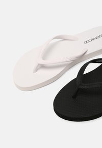 Flip-flops in wit en zwart. Het witte paar heeft een gestructureerde zool en dunne banden; het zwarte paar heeft een gladde afwerking en een vergelijkbaar bandontwerp.