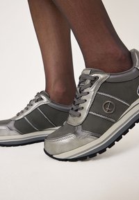Chaussures athlétiques grises avec des accents métalliques, en textile et matériaux synthétiques, design à lacets, semelle robuste et détail du logo sur le côté.