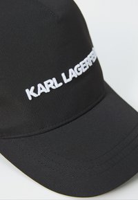Zwarte pet van gestructureerde stof met een witte geborduurde "KARL LAGERFELD" logo op de voorkant en een gebogen vizier met stikaccenten.