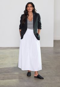 Sort blazer med grønt accent, stribet bluse i hvid og sort, hvid lang nederdel og sorte slip-on sko, sat mod en neutral baggrund.