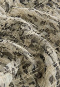 Tissu léger à motifs beige et noir, présentant un aspect texturé froissé avec des plis doux et fluides et un léger éclat.