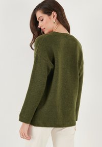 Donkergroen gebreide trui met een losse pasvorm, drop shoulders en een ribgebreide zoom. Soepele textuur met een zachte, casual uitstraling.