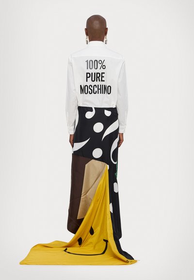 Balta krekla ar uzrakstu "100% PURE MOSCHINO" melnā krāsā aizmugurē, apvienota ar rakstainu, krāsainu svārku, kurā ir dzeltenas, melnas un brūnas daļas.
