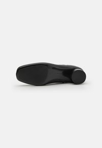 Chaussure à talon noire avec un dessus en cuir lisse et une semelle en caoutchouc texturé ; talon rond avec une base circulaire.