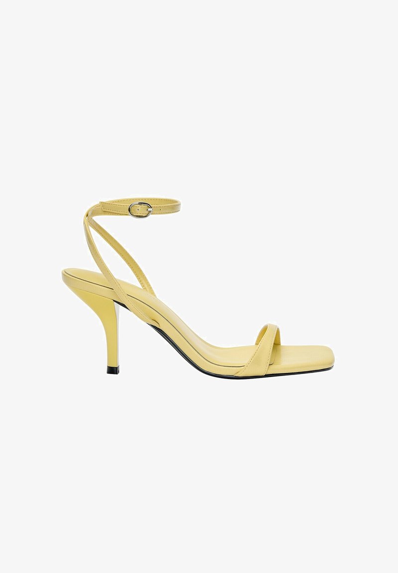 Żółte skórzane sandały na wysokim obcasie typu slingback, z kwadratowym noskiem, cienkim paskiem wokół kostki i błyszczącym wykończeniem, z czarnym akcentem obcasa.