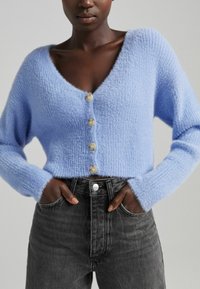 Světle modrý zkrácený kardigan z měkké, strukturované tkaniny s hlubokým V-výstřihem a pěti velkými krémovými knoflíky vpředu.