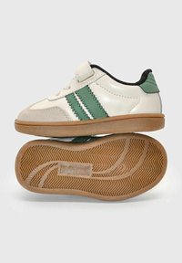 Scarpa da ginnastica bianca e verde per bambini con chiusura a strappo e suola in gomma color gomma, con il nome del marchio impresso nel motivo del battistrada.