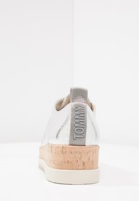 Chaussure métallique argentée avec une plateforme en liège, dotée d'une semelle en caoutchouc grise et d'une languette texturée grise étiquetée "TOMMY" à l'arrière.