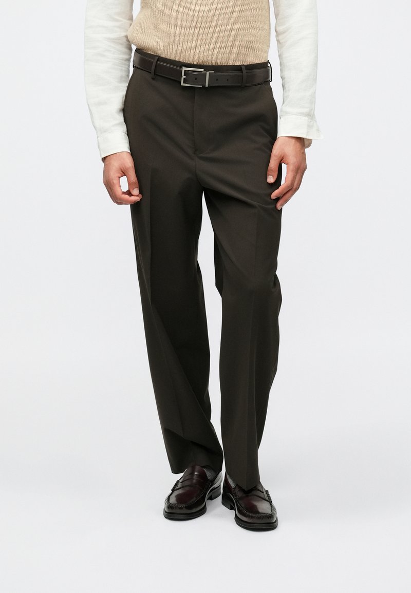 Σκούρες καφέ ψηλόμεσες παντελόνες με ίσια γραμμή, διαθέτοντας μια ζώνη με ορθογώνια ασημένια αγκράφα και λείο υφασμάτινο σχέδιο.