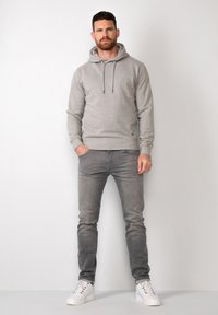 Grijze hoodie met een trekkoord, gecombineerd met lichtgrijze jeans. Witte sneakers maken de outfit af. Soepele stof en slimfit ontwerp.