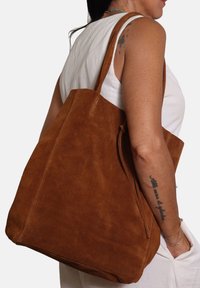 Borsa a tracolla in suede marrone con una texture morbida, design spazioso e lunghe tracolle. Presenta una cucitura minimale e una silhouette semplice.