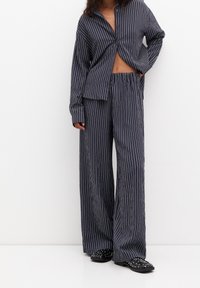 Nawojąsny zestaw odzieży dresowej w paski z kołnierzykiem, zapinany na guziki, oraz spodniami typu wide-leg z elastycznym pasem. Gładka textura materiału.