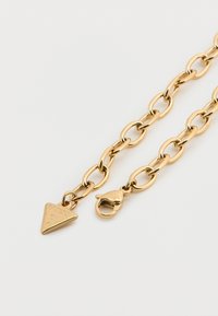 Βραχιόλι με χρυσή αλυσίδα που διαθέτει οβάλ κρίκους, ένα τρίγωνο μενταγιόν με χαραγμένη την επιγραφή "GUESS" και κούμπωμα με κλιπ αστακού.