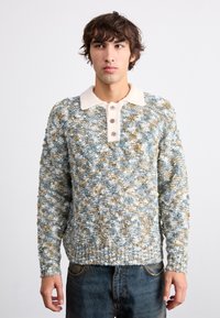 Maglione lavorato a maglia in tonalità blu, bianco e oro. Presenta un colletto color crema e una chiusura a tre bottoni. La texture sembra morbida e soffice.