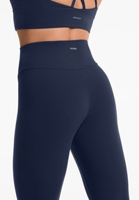 Leggings bleu marine taille haute en tissu extensible. Présentent une texture lisse avec des coutures plates et une taille élastique pour le confort.