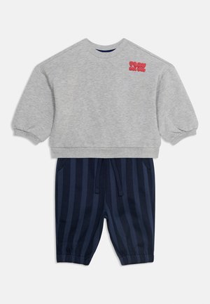Felpa corta grigia a maniche lunghe con scritta rossa "PLAY ALL DAY" abbinata a pantaloni con righe verticali blu navy e nere con coulisse.