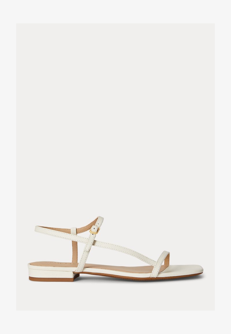 Άσπρο επίπεδο σανδάλι με λεπτές λουρίδες, χρυσή αγκράφα και ανοιχτό σχέδιο στη μύτη, σε ανοιχτό φόντο.