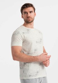 Camiseta de manga corta en color crema con un sutil patrón moteado. Confeccionada en suave algodón, presenta un cuello redondo y un diseño de corte regular.