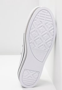 Bílá gumová podešev tenisky s texturovaným geometrickým vzorem a černým akcentovým pruhem. Obsahuje logo značky a označení velikosti na boku.