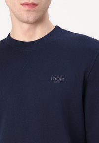 Sudadera azul marino oscura hecha de tela suave, con cuello redondo, puños de canalé y un pequeño logo "JOOP! JEANS" en el pecho.