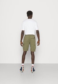 Shorts cargo vert olive avec plusieurs poches, associés à un t-shirt blanc ; portés avec des baskets montantes bleues et des chaussettes rayées.