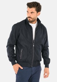 Giacca bomber leggera blu navy con chiusura a zip frontale, tasche laterali, polsini e colletto a costine. Texture liscia, design minimalista.