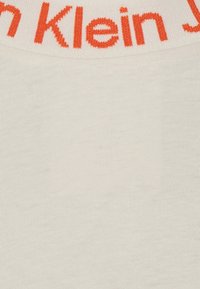 Bílá látka s červeno-oranžovým pleteným textem, který částečně zobrazuje "Klein J" blízko horního okraje.