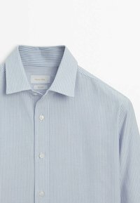 Chemise bleu clair à manches longues avec texture côtelée verticale, col classique et boutons blancs à l'avant.