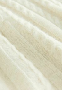 Tissu tricoté de couleur crème avec un motif en côtes et de subtils détails en câble, offrant un aspect doux et texturé.