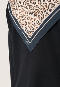 Kvadratisk silketørklæde med leopardprint i beige og brune nuancer, kantet med marineblå og hvide kanter. Signaturen synlig.