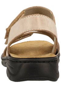 Beige Sandale mit doppelten Stoffriemen, weicher Wildleder-Textur und einer gepolsterten schwarzen Sohle; verfügt über eine offene Ferse und verstellbare Verschlüsse.