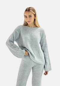 Hellgrauer Strickpullover und passende Hose mit vertikal gerippter Struktur. Übergroße Ärmel und lockere Passform, die eine entspannte Silhouette bietet.