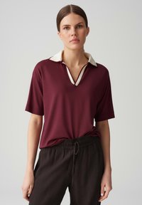 Polo bordeaux avec un col crème et un décolleté en V, associé à un pantalon noir texturé ample avec une taille élastique.