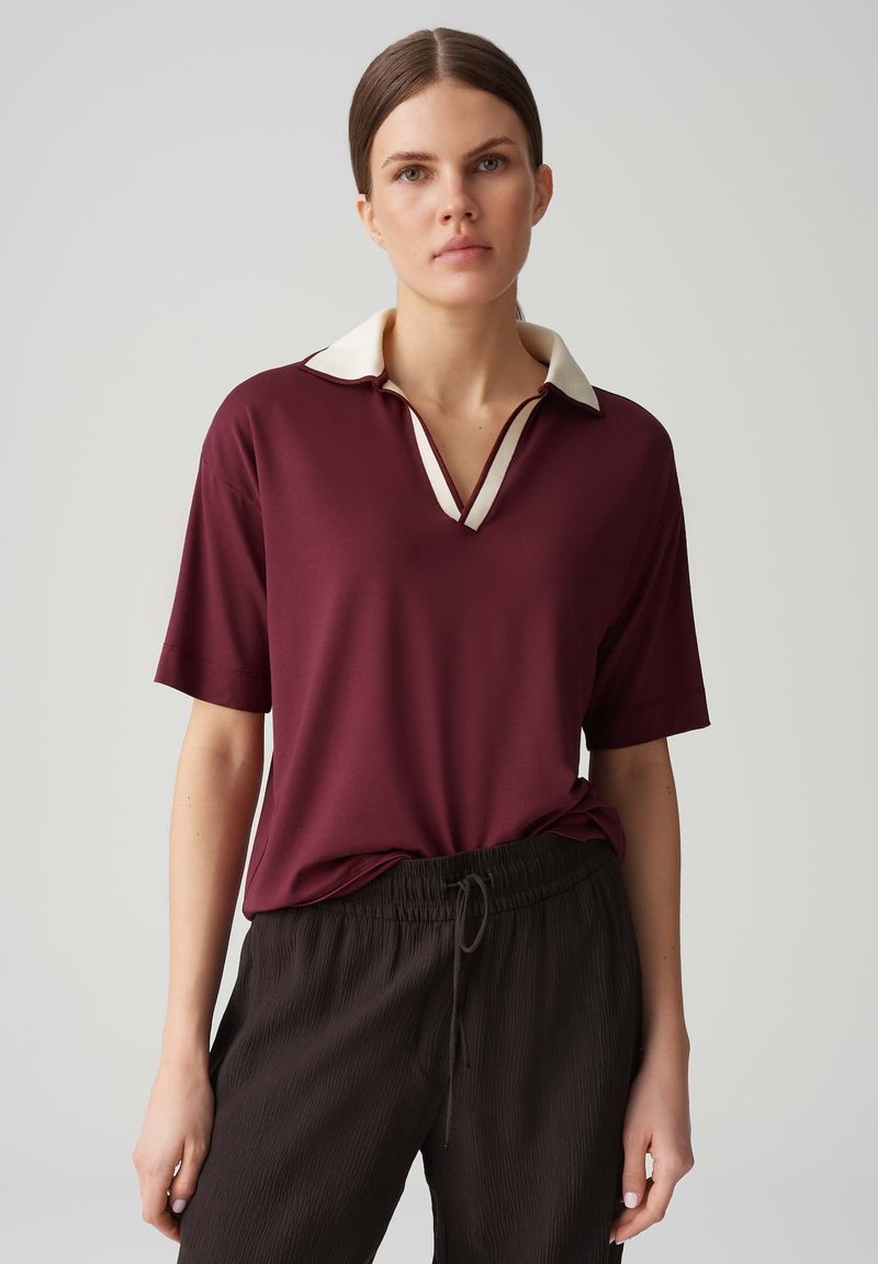 Polo bordeaux avec un col crème et un décolleté en V, associé à un pantalon noir texturé ample avec une taille élastique.