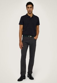 Marineblauwe polo met een contrasterende kraag, grijze broek en zwarte leren laarzen. Het model poseert met een hand in de zak, waarmee het casual outfit wordt getoond.